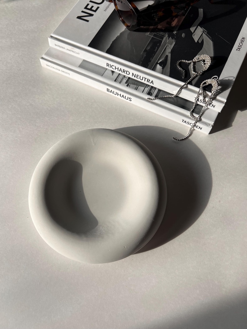 May include: A white ceramic dish with a rounded, slightly raised rim. The dish is sitting on a white surface.