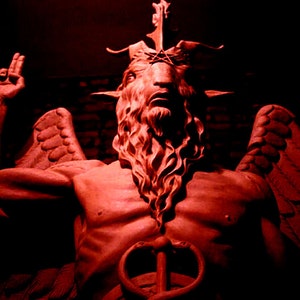 Puede incluir: Una estatua roja de una figura alada y cornuda con barba y corona. La figura sostiene un bastón con una serpiente enroscada alrededor.