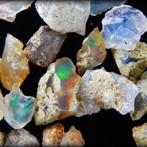 May include: A collection of rough opal stones in various shades of white, brown, and green. The stones have a natural, unpolished look and show iridescent flashes of color.
