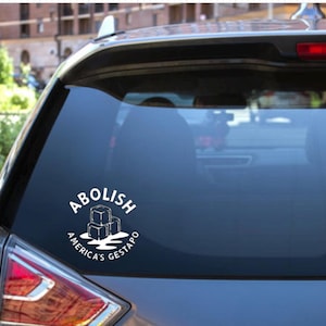 May include: White vinyl car decal with the words "ABOLISH AMERICA'S GESTAPO" in a circular design. The design includes three ice cubes melting. The decal is affixed to the rear window of a black SUV.