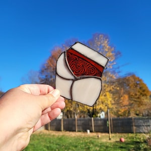 May include: A stained glass window hanging features a white background with a red and white design. The design is a stylized floral pattern.