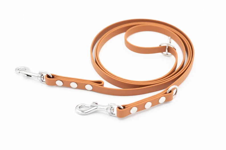 May include: A brown leather dog leash with two silver clips and silver accents. The leash is coiled up on a white background.