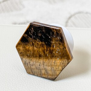 May include: A hexagonal phone grip with a tiger's eye stone design. The stone is brown and gold with a shimmering effect.