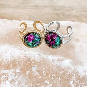 May include: Two adjustable rings with a double band design. The rings feature a round, green and pink gemstone cabochon.