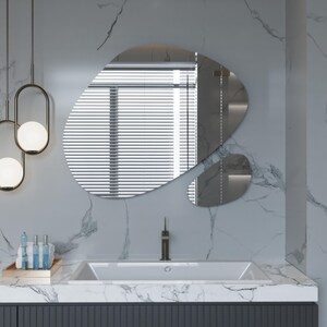 Pu&ograve; includere: Un lavabo in porcellana bianca con un rubinetto unico in un bagno moderno con un piano in marmo bianco e uno specchio di forma organica.