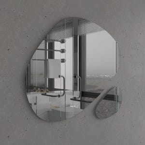 Pu&ograve; includere: Uno specchio da bagno moderno con una forma irregolare e organica. Lo specchio riflette una vista di un bagno con un portasciugamani, una finestra e un lavandino.