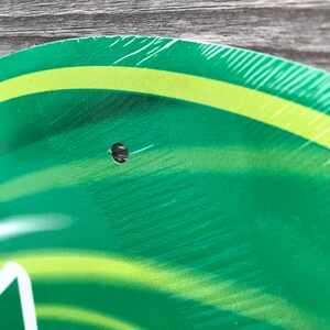 May include: Green and yellow round sign with a hole in the center. The sign has a swirl pattern.