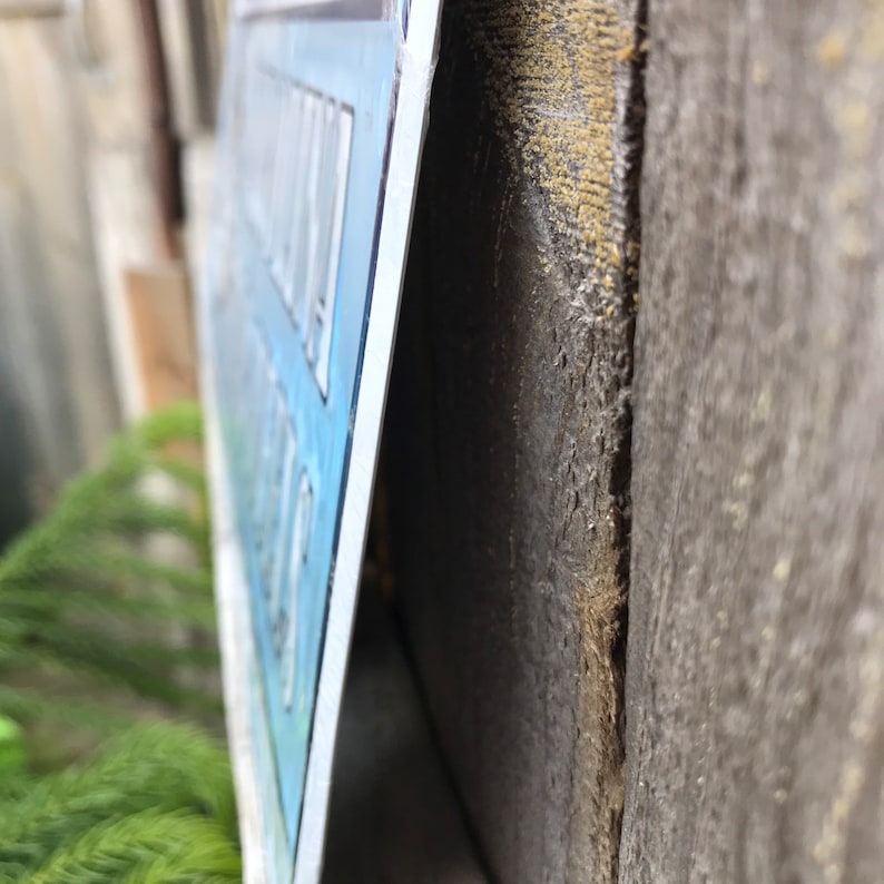 May include: A close-up of a blue and white sign with the text "Welcome to Our Home" hanging on a wooden wall.