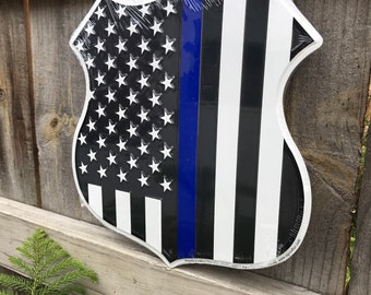 May include: A metal sign in the shape of a US highway shield with an American flag design and a blue line running down the center. The sign is black, white, and blue.