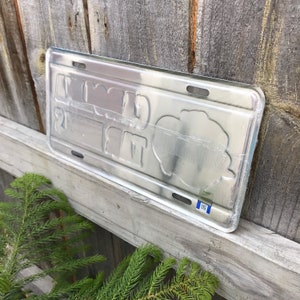 May include: A silver metal license plate with the text "World's Greatest Dad" printed on it. The plate has a blue border and a small blue sticker with the text "Made in USA" on the bottom right corner.