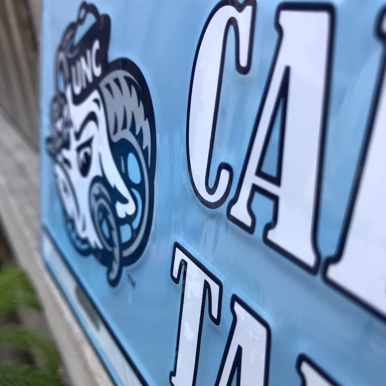 May include: A light blue metal sign with the word "CAR" in white letters and a cartoon ram mascot with the letters "UNC" on its hat.