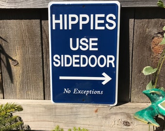 May include: Blue sign with white text that reads "Hippies Use Sidedoor No Exceptions" with a white arrow pointing to the right.