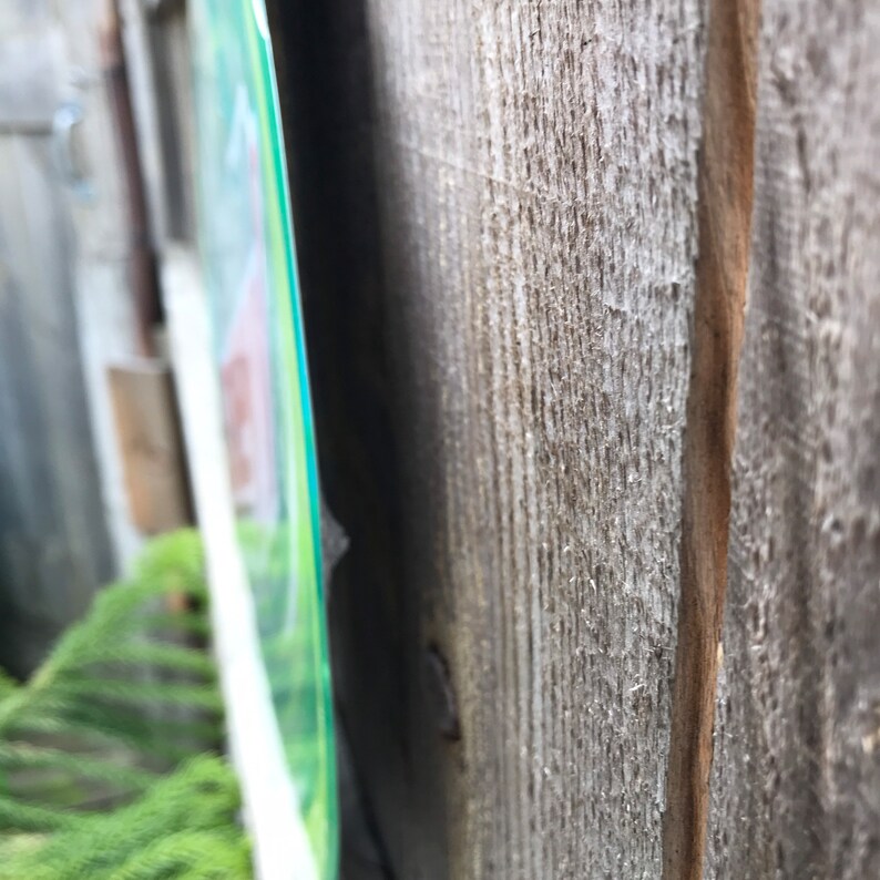 May include: A close-up of a wooden fence with a green and white sign attached to it. The sign is partially obscured by the fence.
