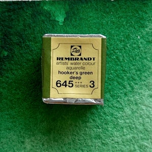 May include: A small, rectangular, silver-colored tin of Rembrandt artists' water color in the shade Hooker's Green Deep. The tin is labeled with the brand name, color name, and number 645 Series 3.