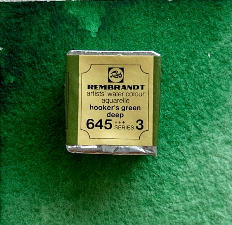 May include: A small, rectangular, silver-colored tin of Rembrandt artists' water color in the shade Hooker's Green Deep. The tin is labeled with the brand name, color name, and number 645 Series 3.