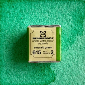 May include: A small, rectangular tin of emerald green watercolor paint. The tin is labeled "REMBRANDT artists' water colour aquarelle emerald green 615 +++ SERIES 2".