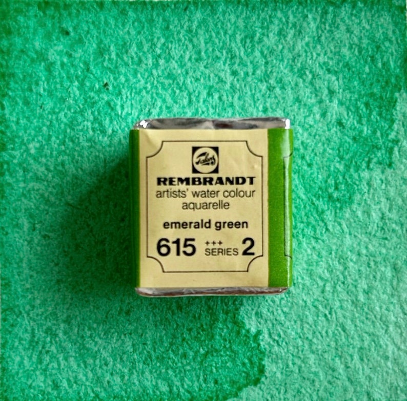 May include: A small, rectangular tin of emerald green watercolor paint. The tin is labeled "REMBRANDT artists' water colour aquarelle emerald green 615 +++ SERIES 2".