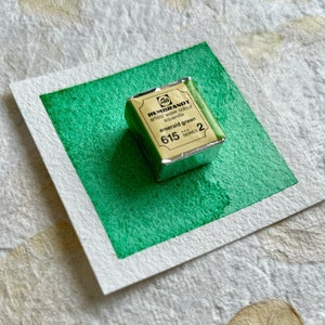 May include: A small, silver-colored pan of emerald green watercolor paint. The pan is labeled "Rembrandt artist's water colour" and "emerald green 615 series 2".