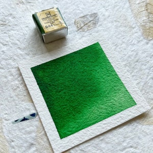 Puede incluir: Una peque&ntilde;a bandeja de pintura de acuarela Winsor & Newton de color plateado. La etiqueta dice "Winsor & Newton Artists' Water Colour, Hooker's Green Light, 644, 3.5 ml Tubes". La pintura es de un verde vibrante.