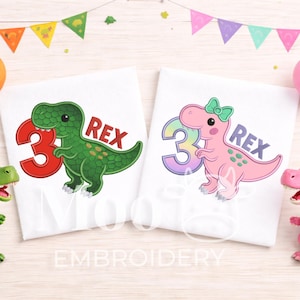 May include: Two white t-shirts with dinosaur graphics. One shirt features a green dinosaur with the number 3 in red and the name "REX". The other shirt has a pink dinosaur with a bow, a number 3 in pastel colors, and the name "REX".