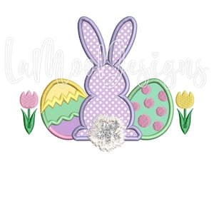 May include: Purple bunny with a white fluffy tail sitting between three Easter eggs. The eggs are green, yellow, and pink with white polka dots.