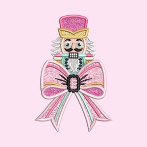 May include: A pink and white glitter bow with a nutcracker face in the center. The nutcracker is wearing a blue and gold hat and has a white beard.