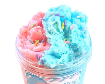 May include: A clear plastic container filled with pink and blue fluffy slime, resembling cotton candy. The slime is decorated with colorful sprinkles. The container has a label that reads "Cotton Candy" with a graphic of a heart-shaped candy.