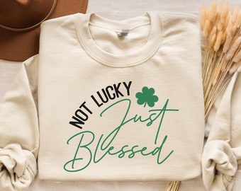 May include: A beige sweatshirt with the text "Not Lucky Just Blessed" in black and green lettering. A green shamrock is included in the design.