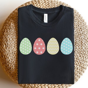 May include: Black t-shirt with four colorful Easter eggs printed on the front. The eggs are decorated with polka dots, stars, zigzags, and hearts.