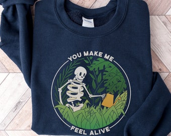 May include: Navy blue sweatshirt with a graphic of a skeleton watering plants. The graphic is surrounded by a circle with the text "You make me feel alive".