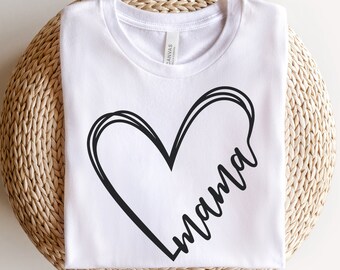 May include: White t-shirt with a black heart design and the word "mama" in a handwritten font. The shirt is folded and placed on a round, woven wicker surface. The shirt is made of a soft, comfortable material.