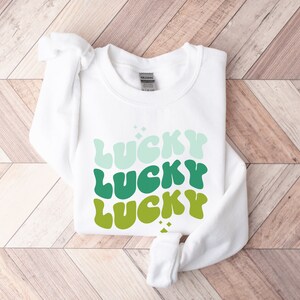 May include: White sweatshirt with the word "LUCKY" repeated three times in a gradient of green, blue, and white.