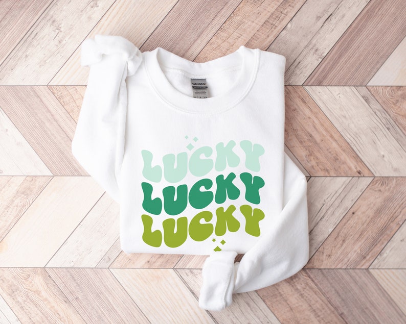 May include: White sweatshirt with the word "LUCKY" repeated three times in a gradient of green, blue, and white.