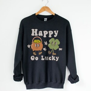 May include: Black sweatshirt with a graphic of a pot of gold and a four-leaf clover with the text "Happy Go Lucky".