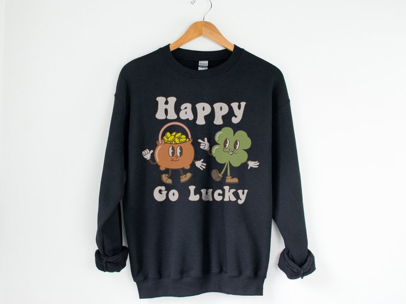 May include: Black sweatshirt with a graphic of a pot of gold and a four-leaf clover with the text "Happy Go Lucky".
