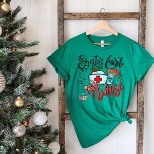 May include: Green t-shirt with a Christmas-themed design that says "Santa's favorite nurse" with a stethoscope, a nurse's hat, a bandage, a gift box, and a cup of coffee with a Santa hat on top.