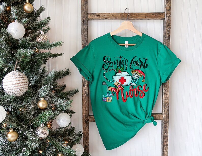 May include: Green t-shirt with a Christmas-themed design that says "Santa's favorite nurse" with a stethoscope, a nurse's hat, a bandage, a gift box, and a cup of coffee with a Santa hat on top.