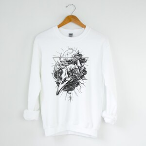 May include: White sweatshirt featuring a black and white graphic print of a skull with a snake wrapped around it. The skull is surrounded by a triangle and stars.