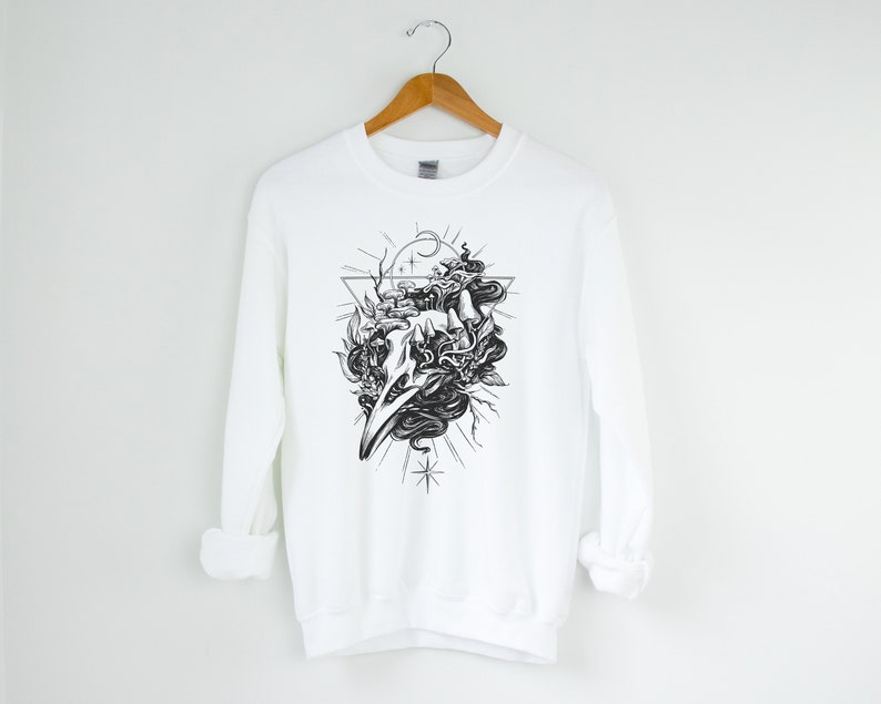 May include: White sweatshirt featuring a black and white graphic print of a skull with a snake wrapped around it. The skull is surrounded by a triangle and stars.