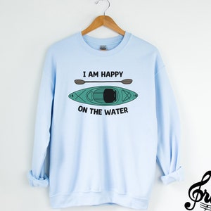 May include: Light blue sweatshirt with a graphic of a kayak and paddles, and the text "I am happy on the water".