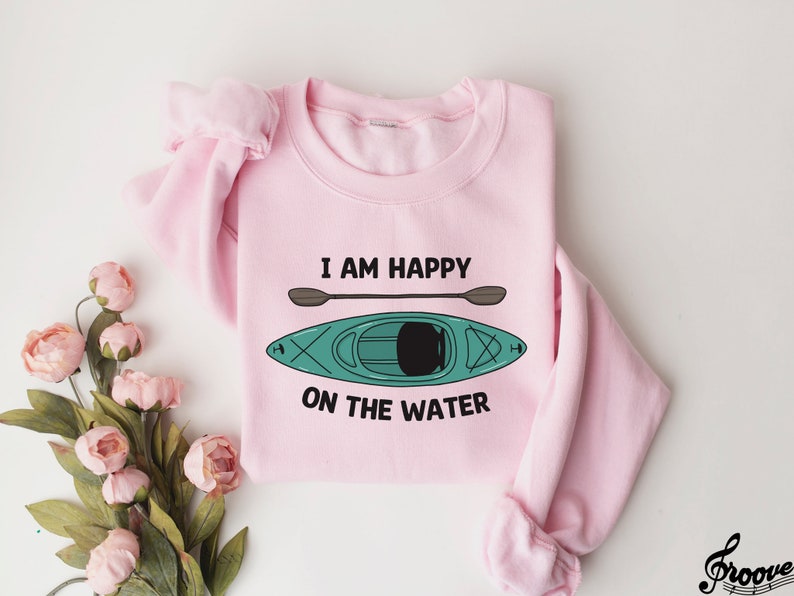 May include: Pink sweatshirt with a graphic of a kayak and paddles. The text "I am happy on the water" is printed on the sweatshirt.