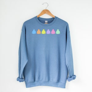 Peut inclure: Un sweat-shirt bleu avec une rang&eacute;e de cinq guimauves en forme de poussins pastel imprim&eacute;es sur le devant.