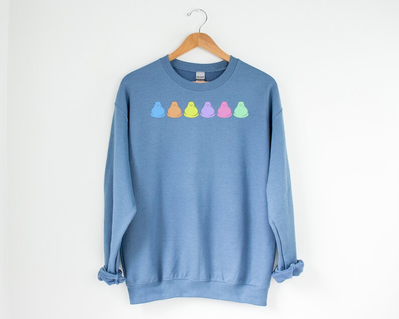 Peut inclure: Un sweat-shirt bleu avec une rang&eacute;e de cinq guimauves en forme de poussins pastel imprim&eacute;es sur le devant.