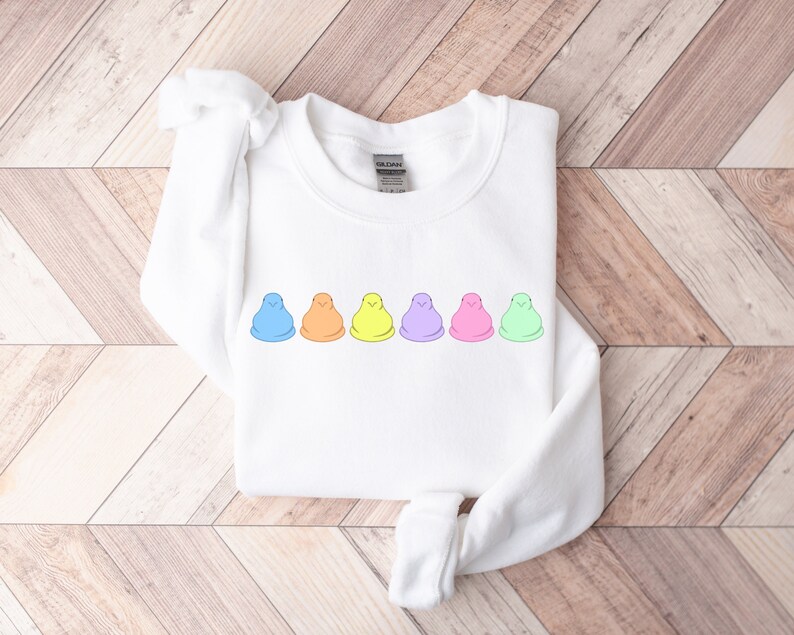 Peut inclure: Sweat-shirt blanc avec une rang&eacute;e de six guimauves en forme de poussins de couleur pastel imprim&eacute;es sur le devant.
