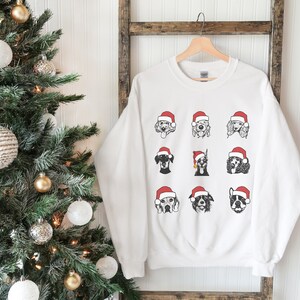 May include: White Christmas sweatshirt with a graphic of nine dogs wearing Santa hats. The dogs are all different breeds and are arranged in a grid pattern.