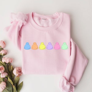 Peut inclure: Un sweat-shirt rose avec une rang&eacute;e de six guimauves color&eacute;es imprim&eacute;es sur le devant.
