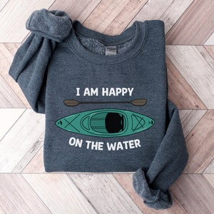 May include: A dark gray sweatshirt with the text "I am happy on the water" and a cartoon image of a green kayak with a brown paddle.