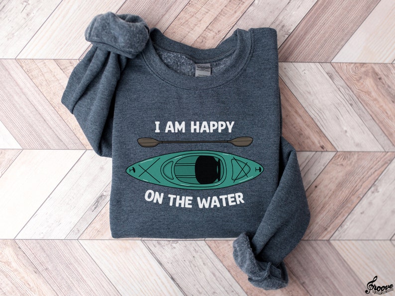 May include: A dark gray sweatshirt with the text "I am happy on the water" and a cartoon image of a green kayak with a brown paddle.