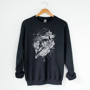 May include: Black sweatshirt with a white graphic print of a skull with smoke and stars inside a triangle.