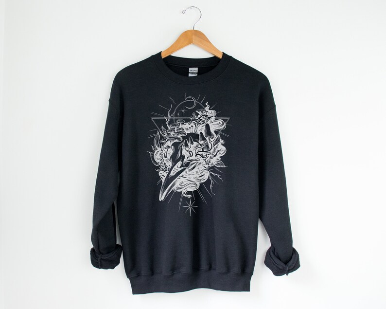 May include: Black sweatshirt with a white graphic print of a skull with smoke and stars inside a triangle.